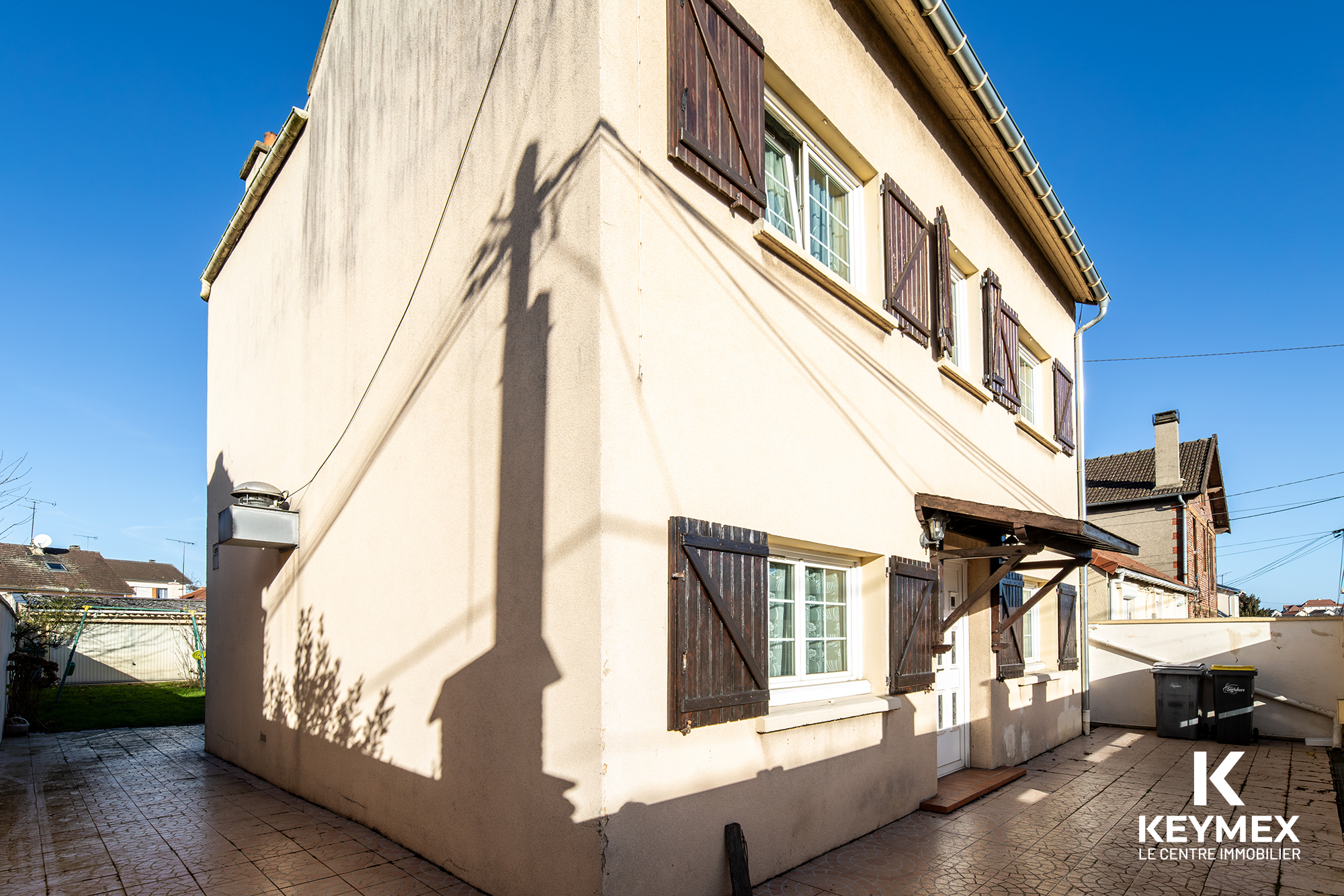 Façade de maison avec volets en bois, ciel bleu.