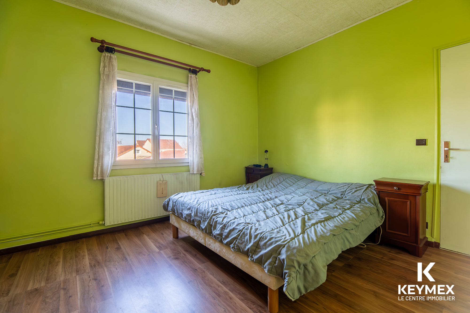 Chambre lumineuse avec murs verts et parquet bois