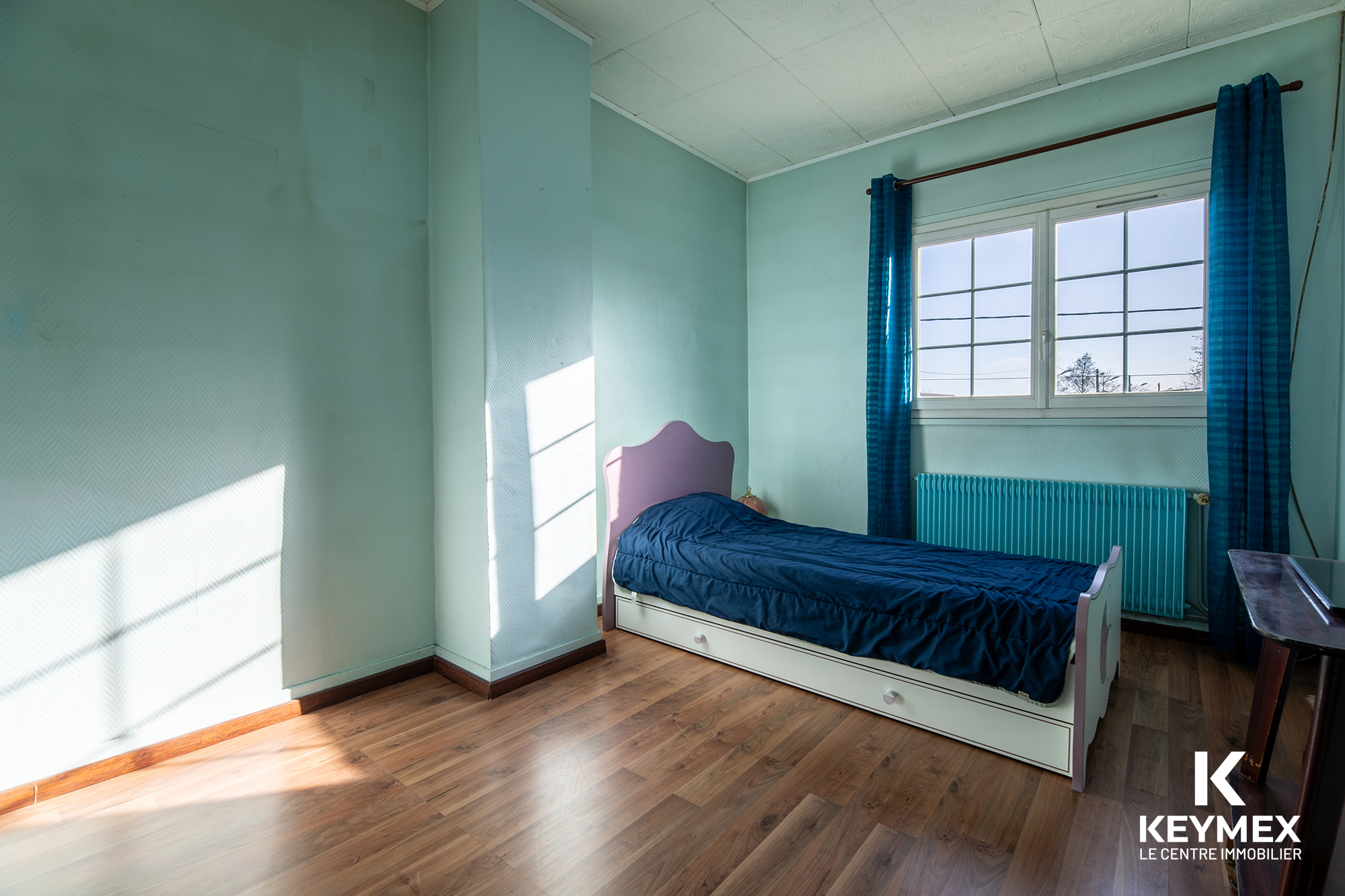 Chambre lumineuse avec lit simple et parquet bois.