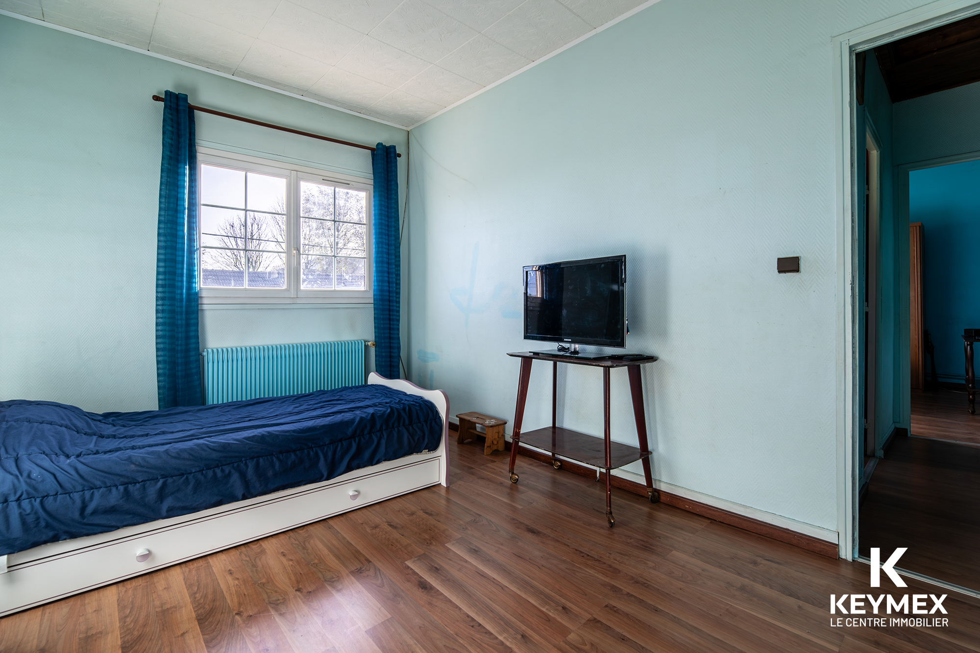 Chambre avec lit simple et télévision, décoration bleue.