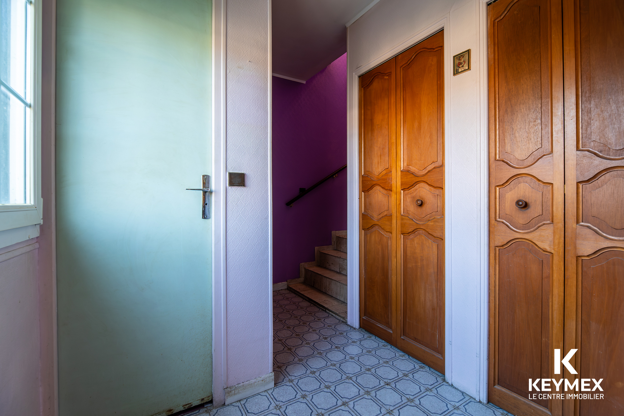 Entrée avec porte turquoise, placard en bois, escalier violet.