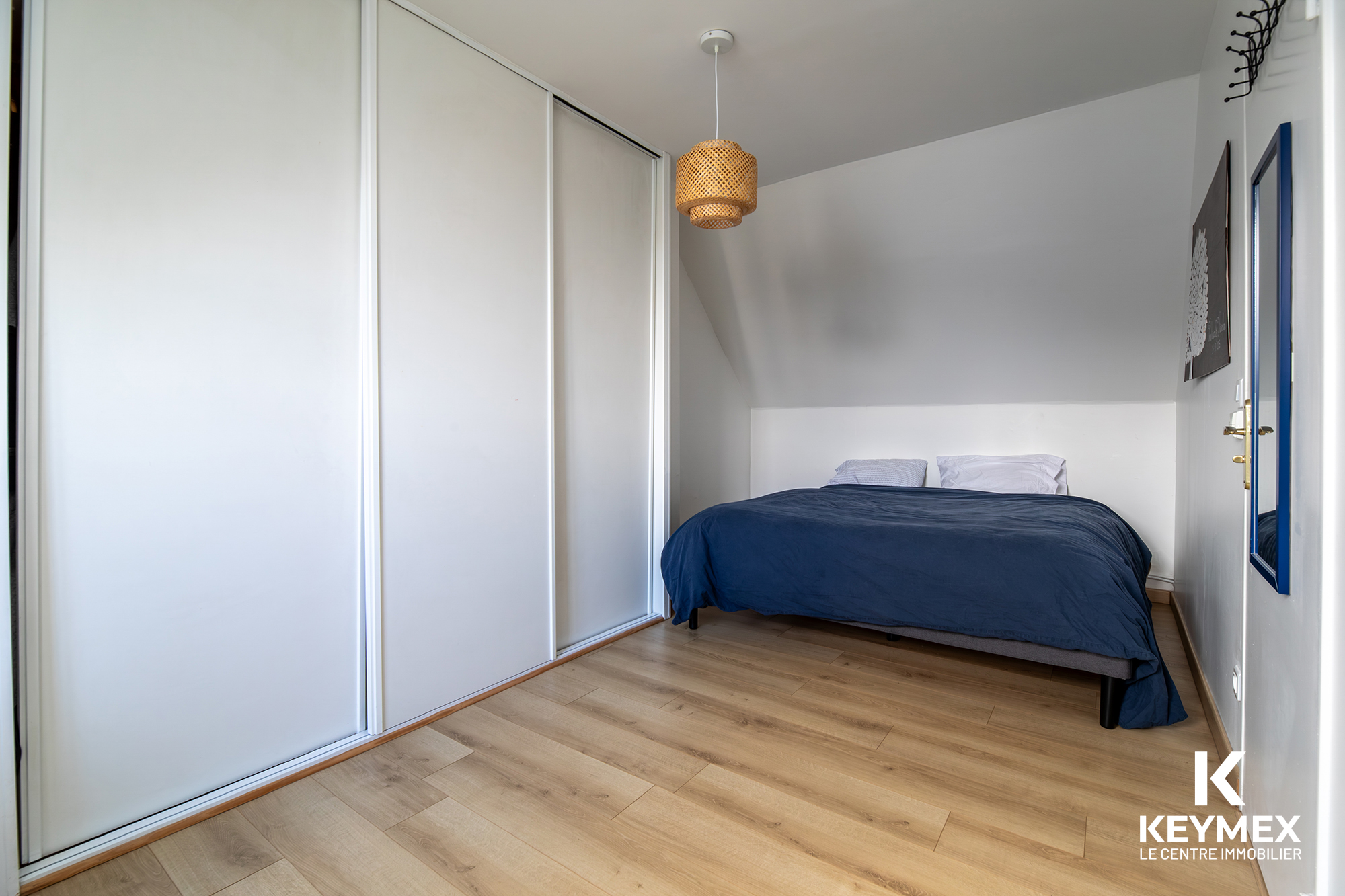 Chambre lumineuse avec lit et parquet clair.