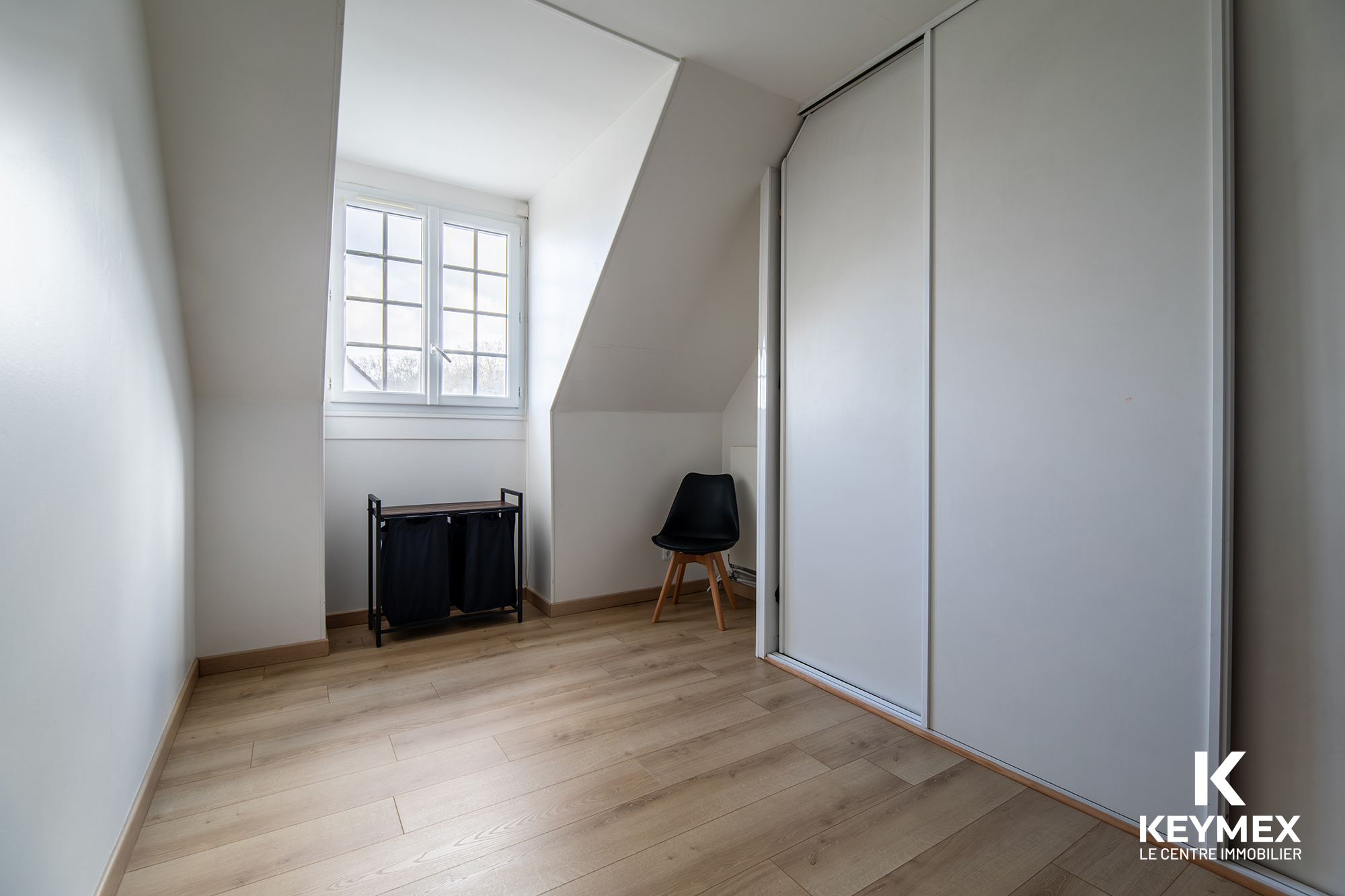 Petite chambre mansardée lumineuse avec sol en bois.