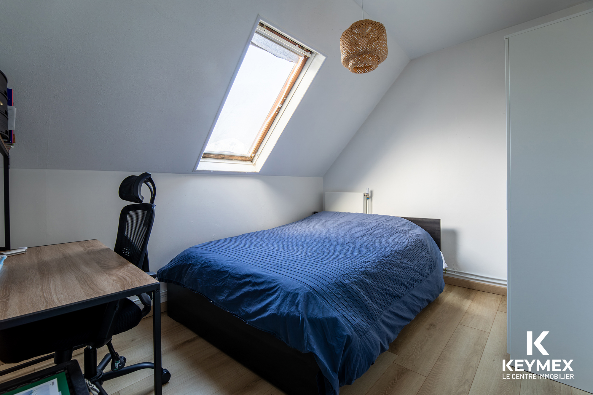 Chambre mansardée avec bureau et fenêtre de toit.