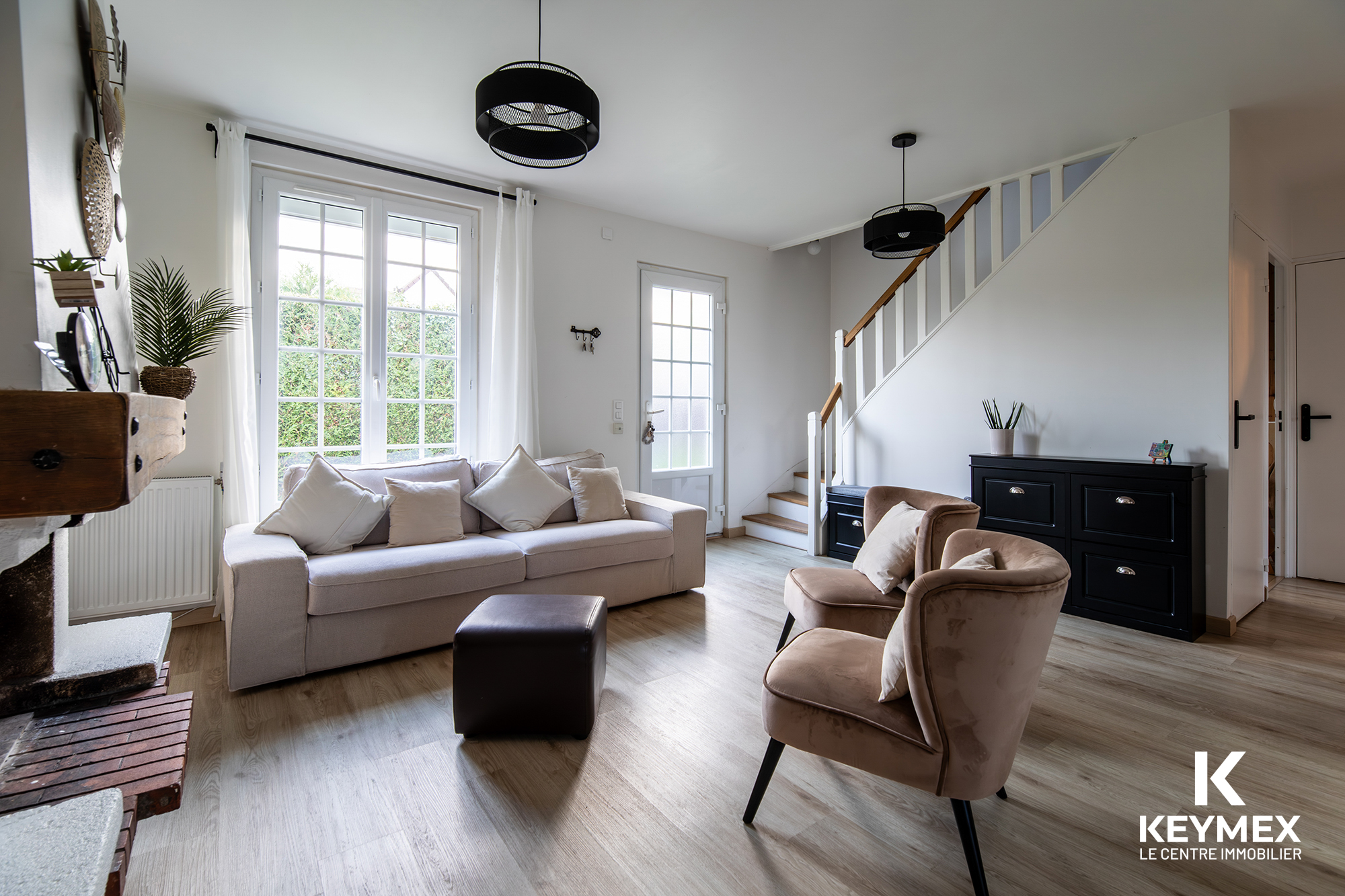 Salon moderne avec canapé beige et escalier blanc.