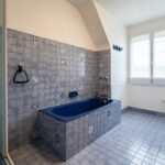 Salle de bain avec baignoire bleue et carrelage gris.