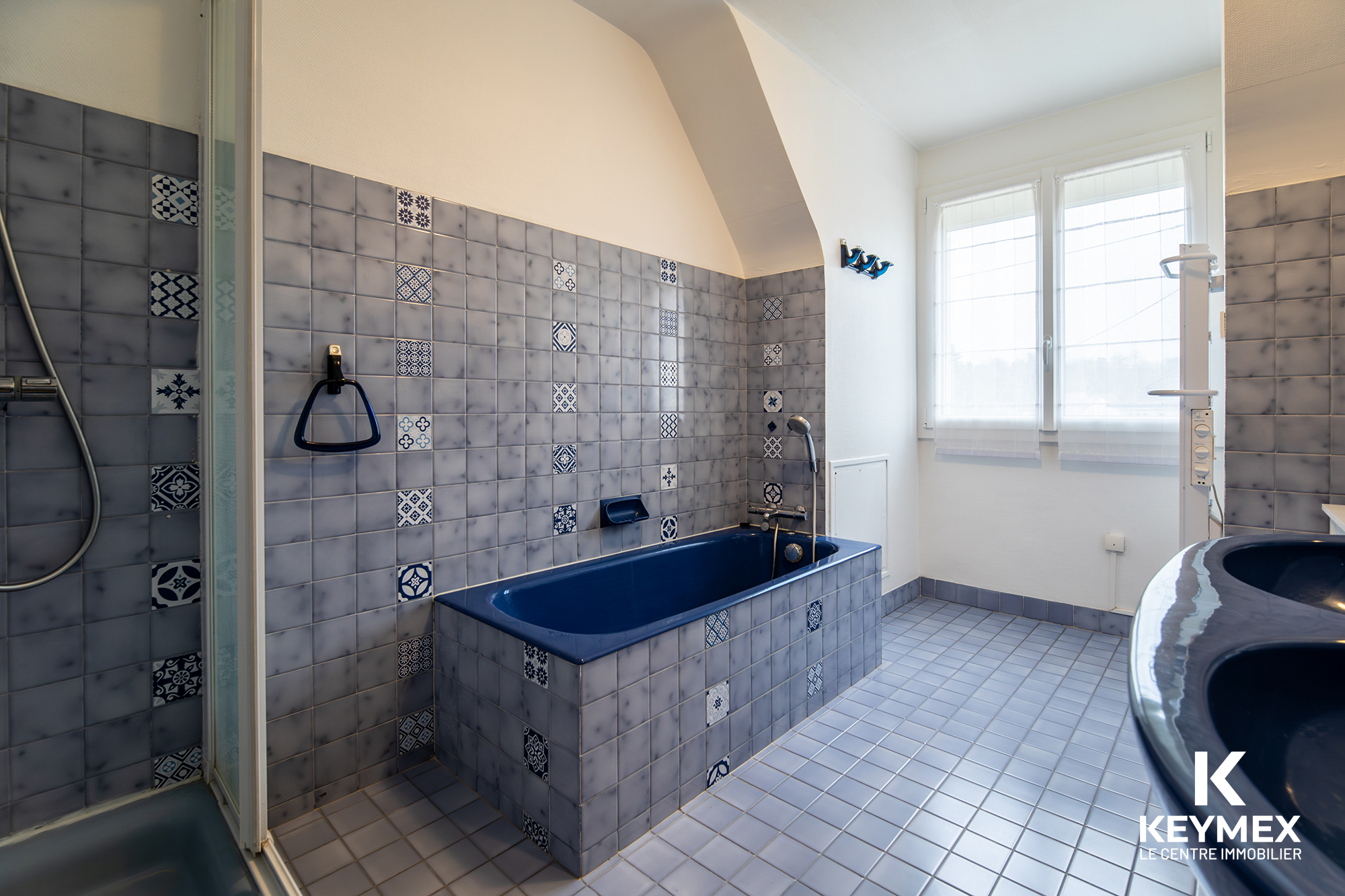 Salle de bain avec baignoire bleue et carrelage gris.