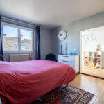 Chambre lumineuse avec lit rouge et parquet en bois.