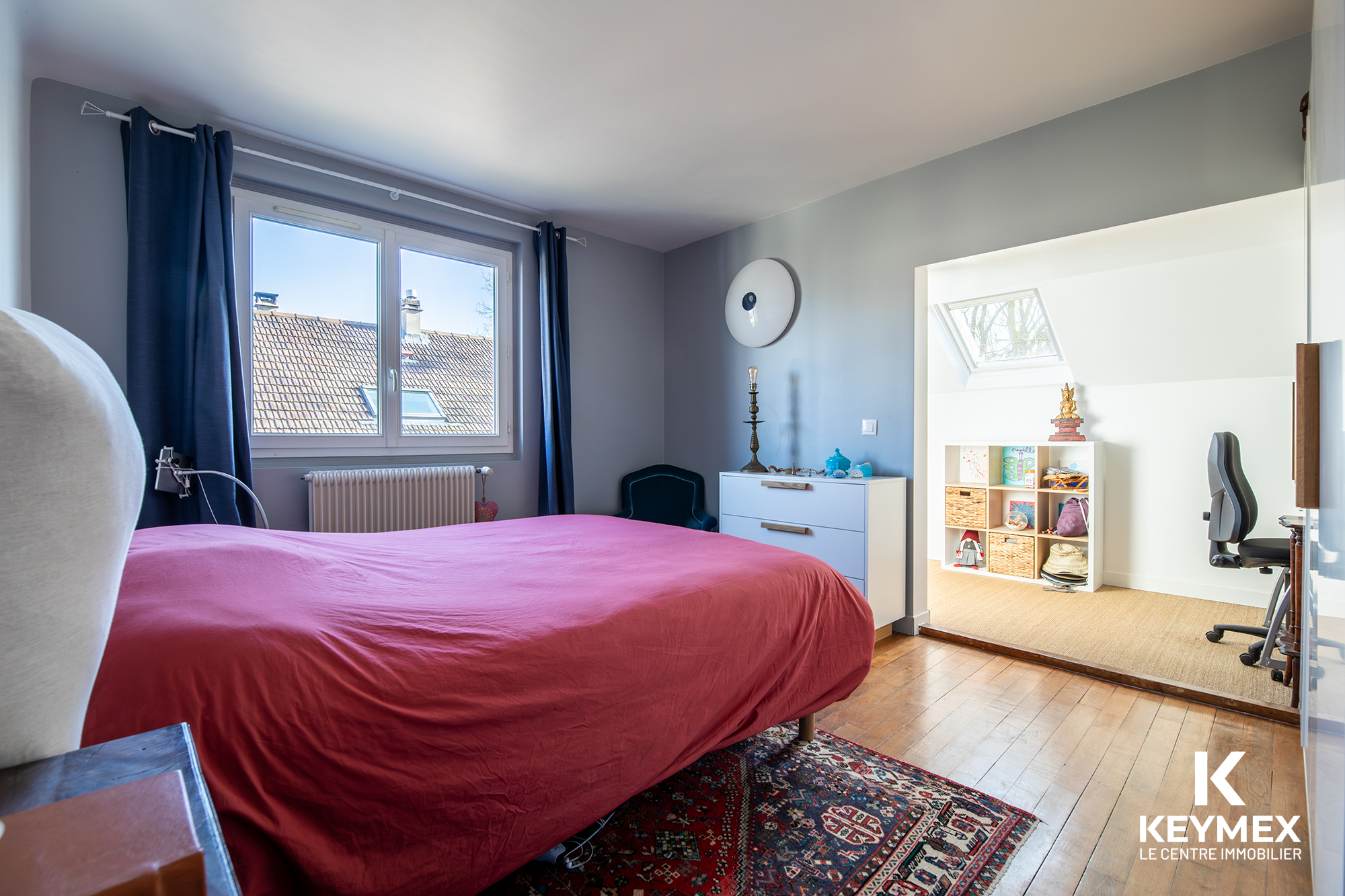 Chambre lumineuse avec lit rouge et parquet en bois.