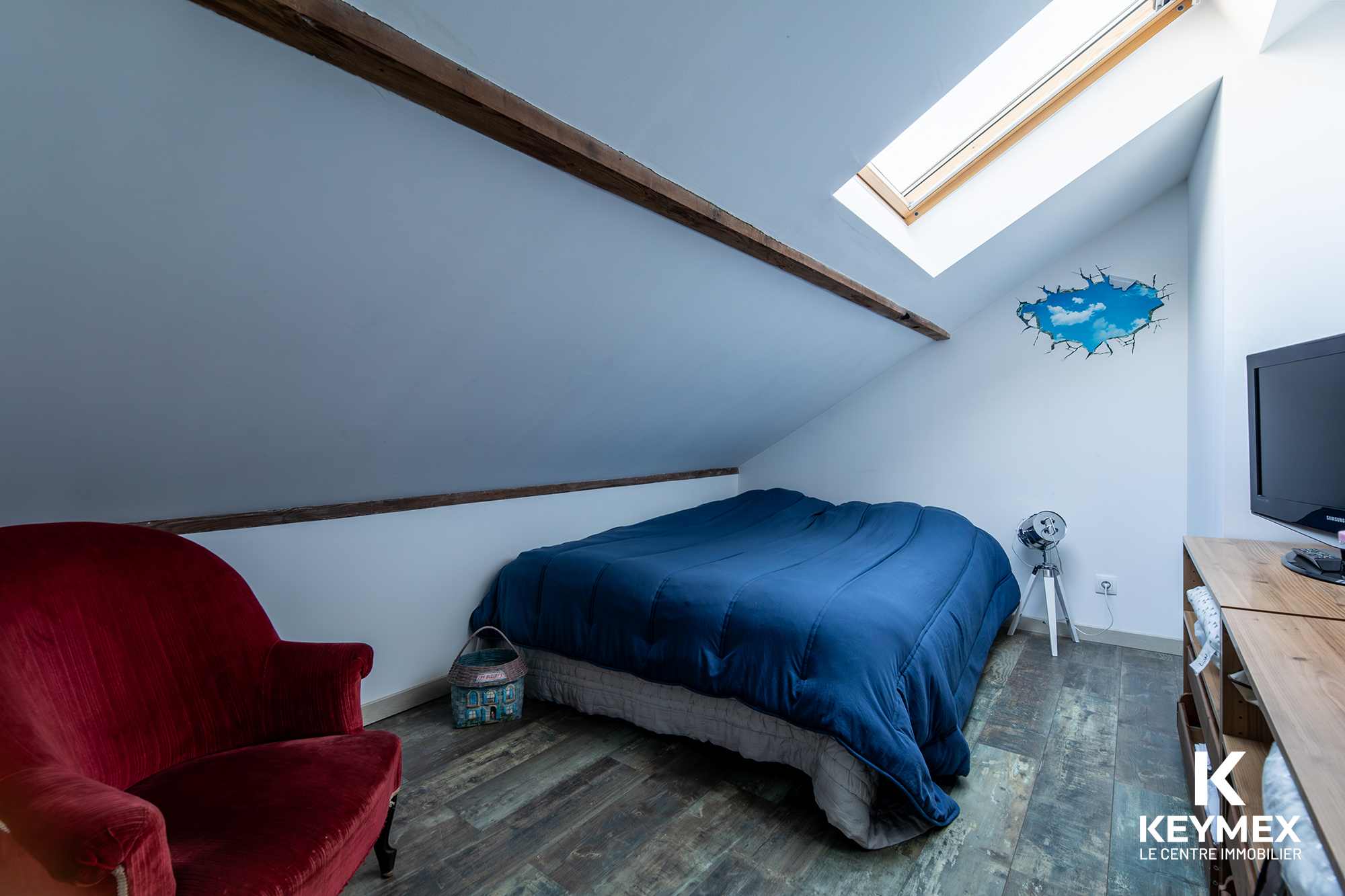 Chambre mansardée avec lit et fauteuil rouge.