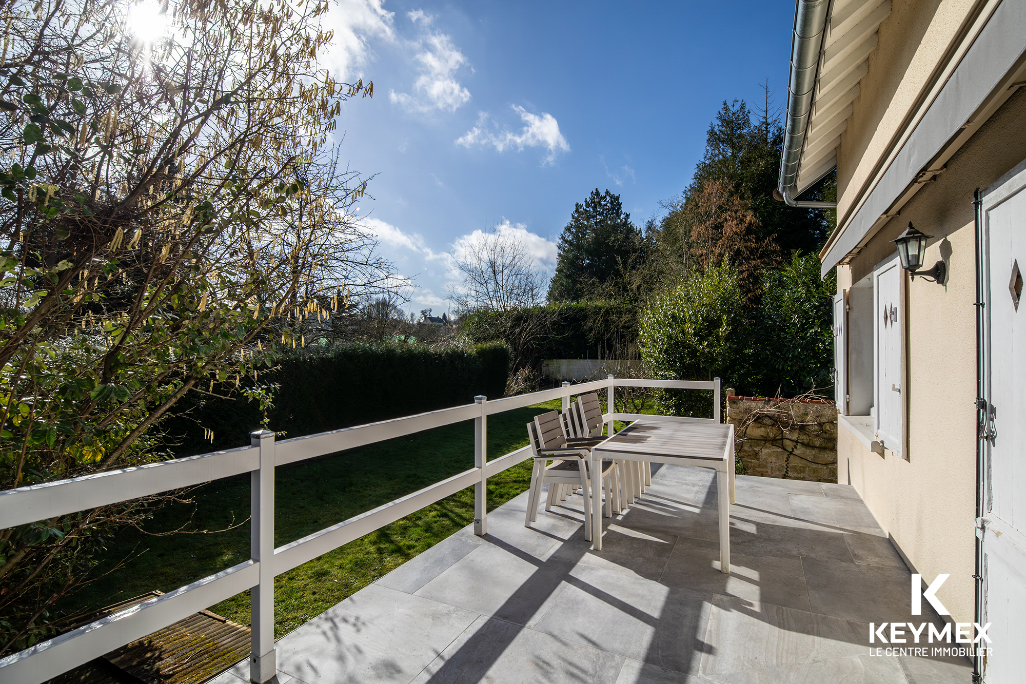 Terrasse ensoleillée avec table et chaises blanches.