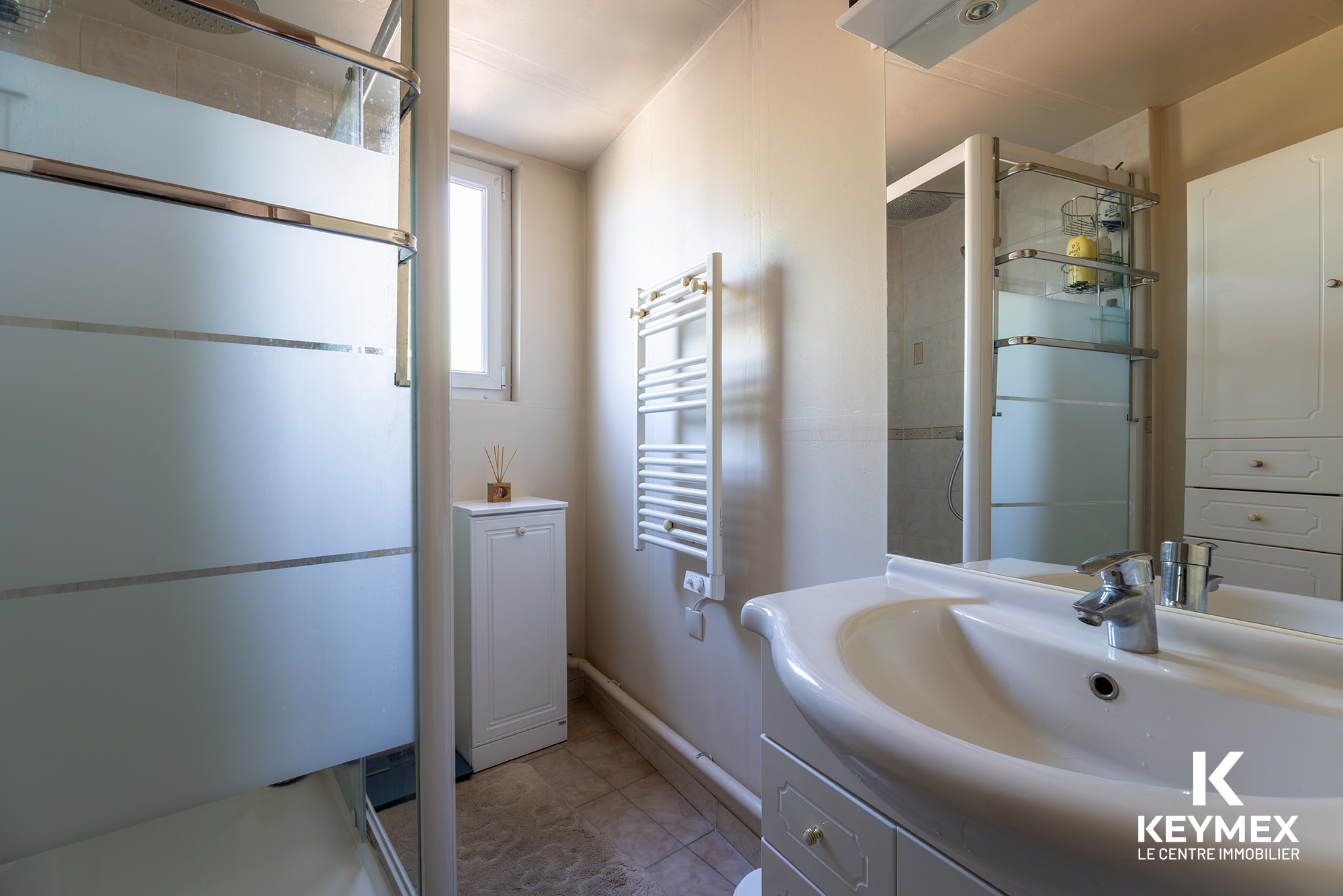 Salle de bain moderne avec douche et lavabo blancs.