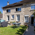 Maison en pierre avec jardin, ciel bleu dégagé.