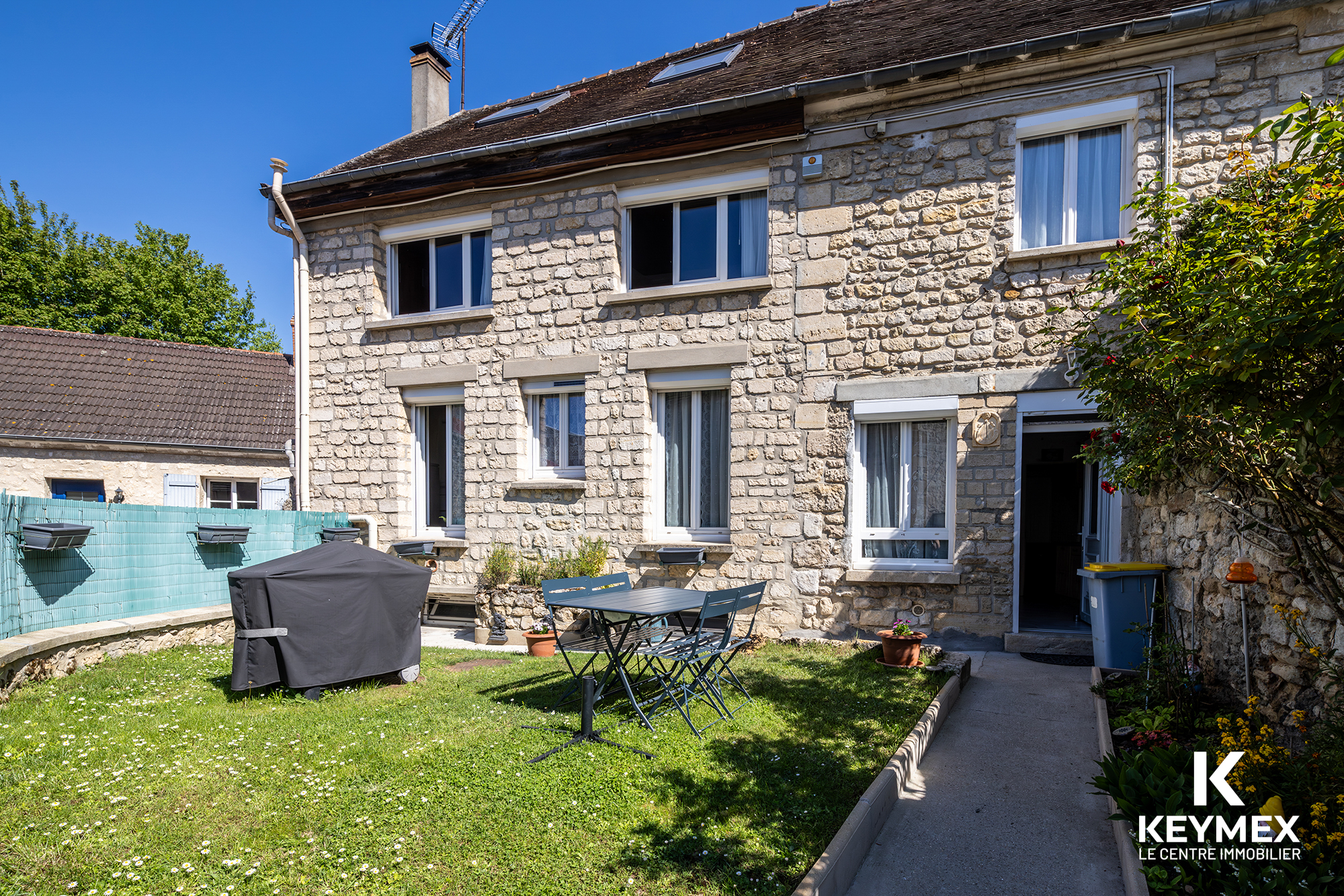 Maison en pierre avec jardin, ciel bleu dégagé.