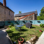 Jardin clôturé avec table et barbecue, maisons en pierre.