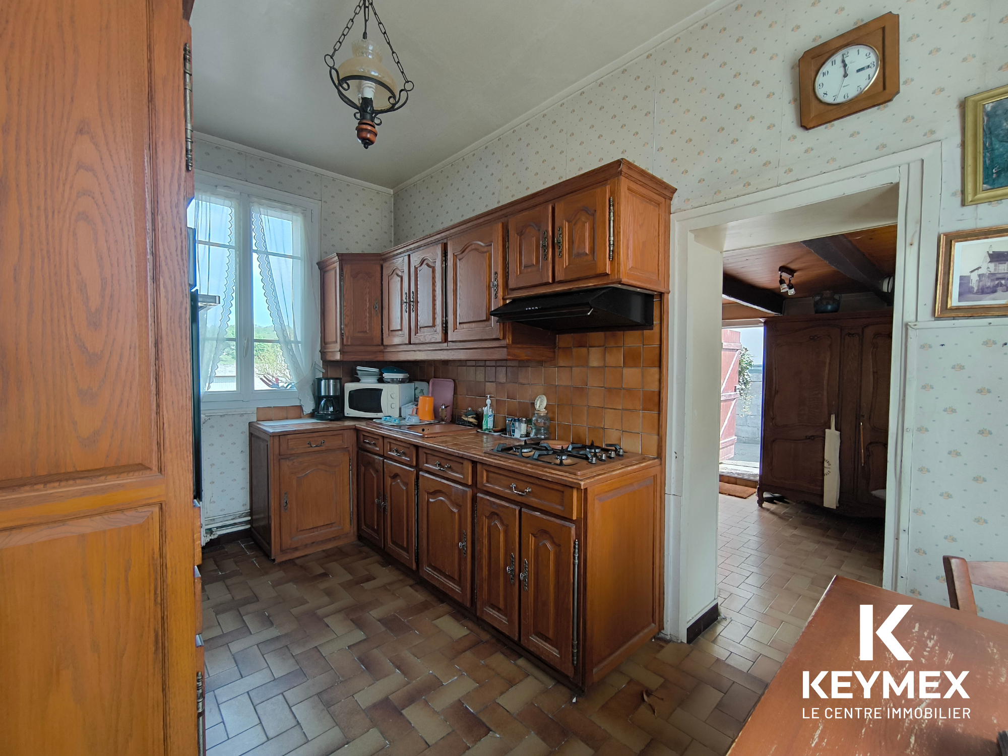 Cuisine ancienne avec meubles en bois et carrelage marron.