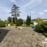 Jardin avec bancs et arbres, ciel bleu dégagé.
