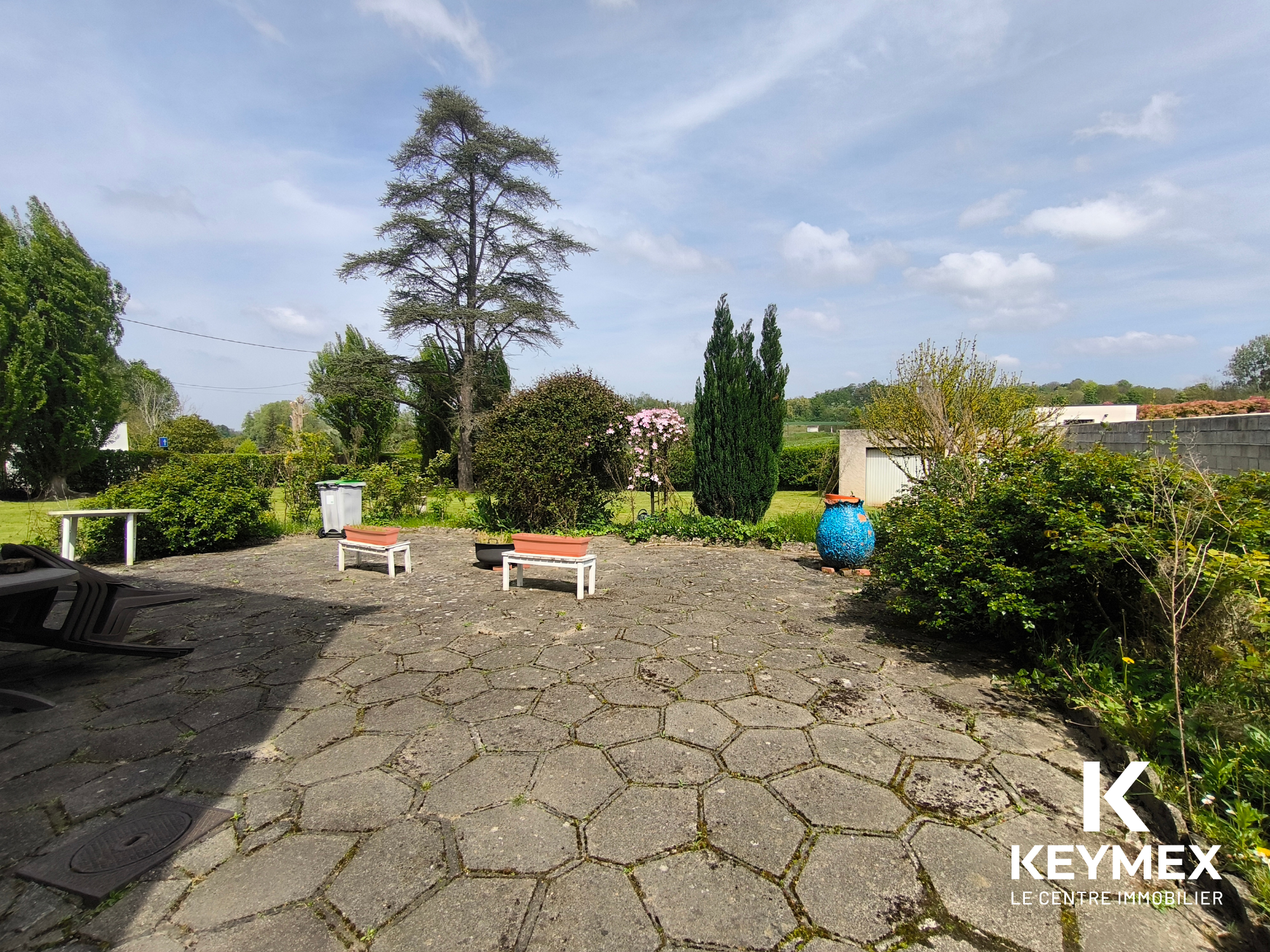 Jardin avec bancs et arbres, ciel bleu dégagé.