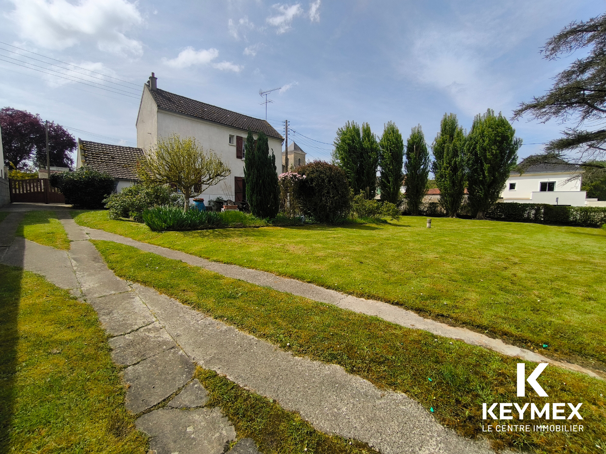 Jardin verdoyant avec maison et allée en béton.