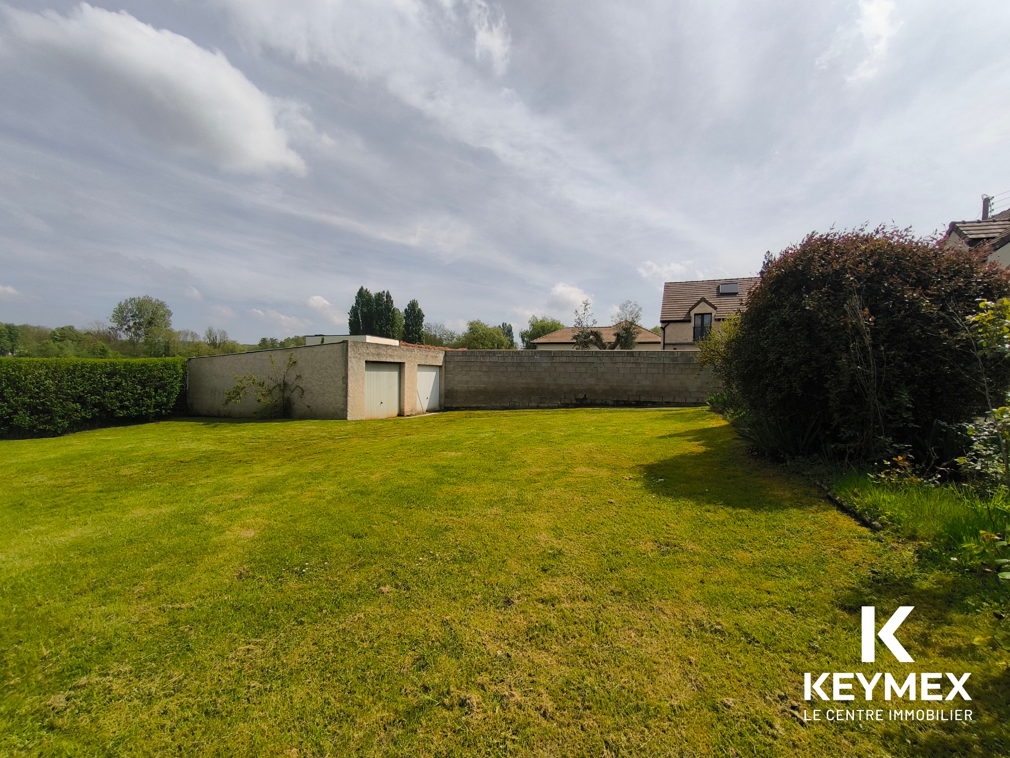 Jardin avec garage et mur en briques.