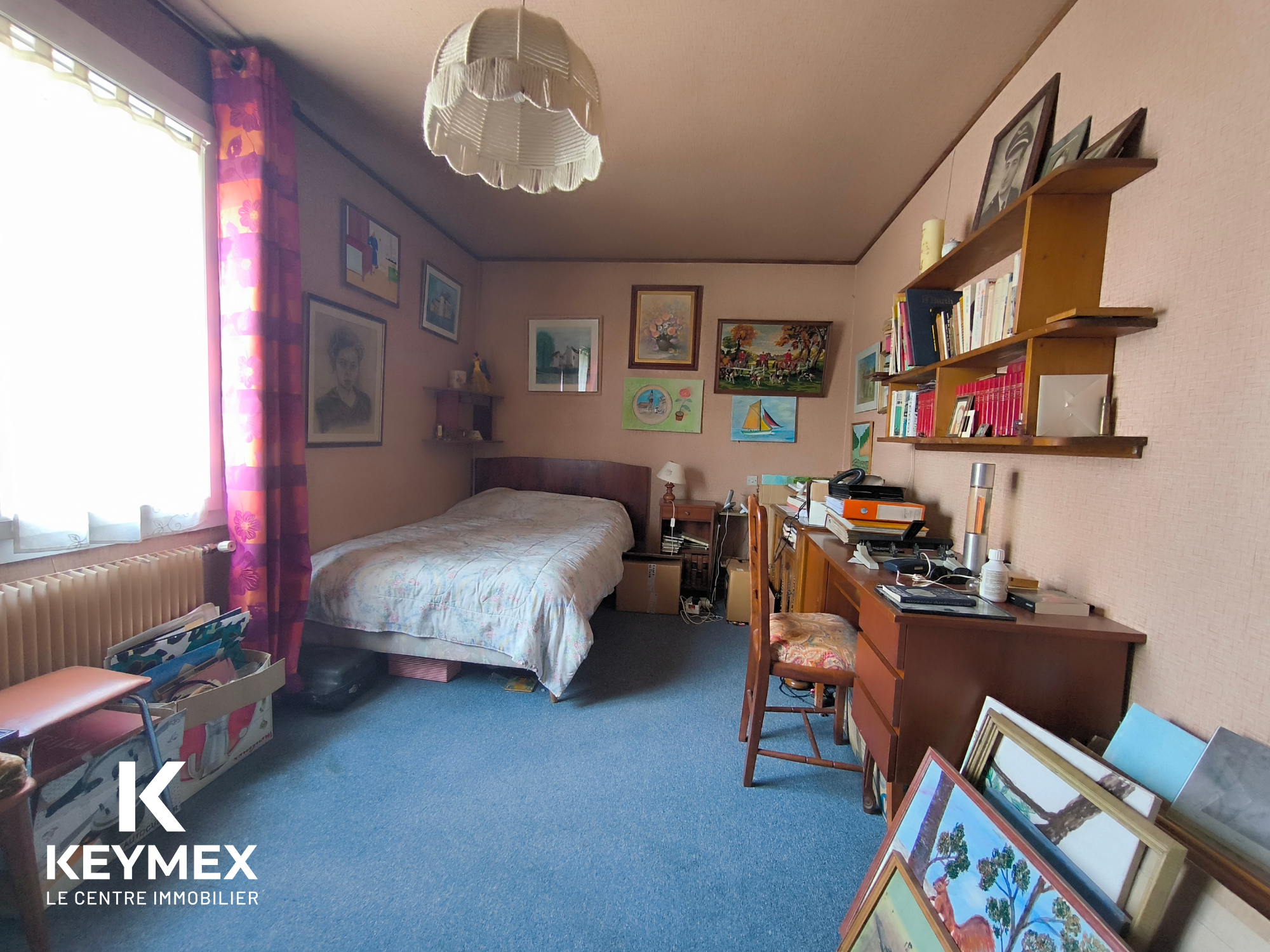 Chambre avec bureau, décorée de tableaux et étagères.