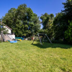 Jardin avec balançoire et maison en fond.