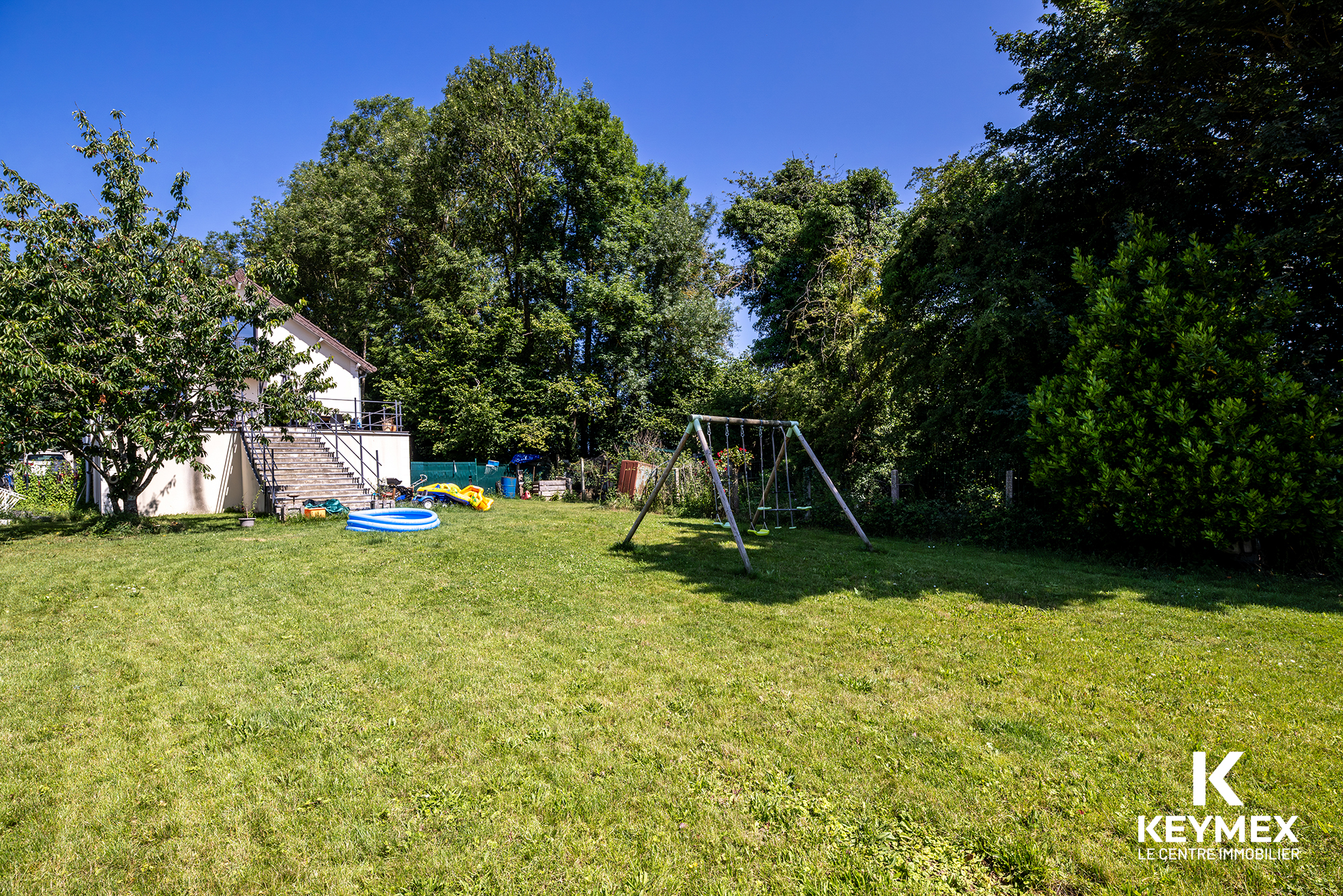 Jardin avec balançoire et maison en fond.