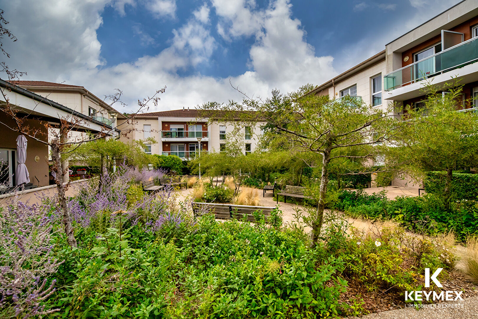 Jardin résidentiel verdoyant avec bancs et immeubles.