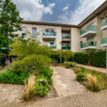 Jardin devant un immeuble moderne avec balcons.