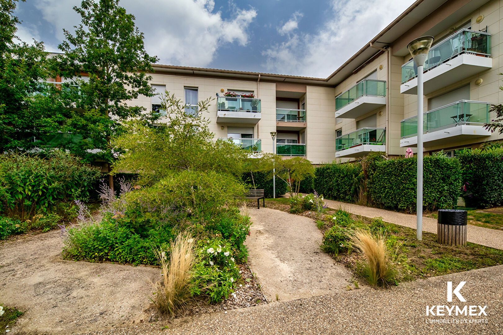 Jardin devant un immeuble moderne avec balcons.