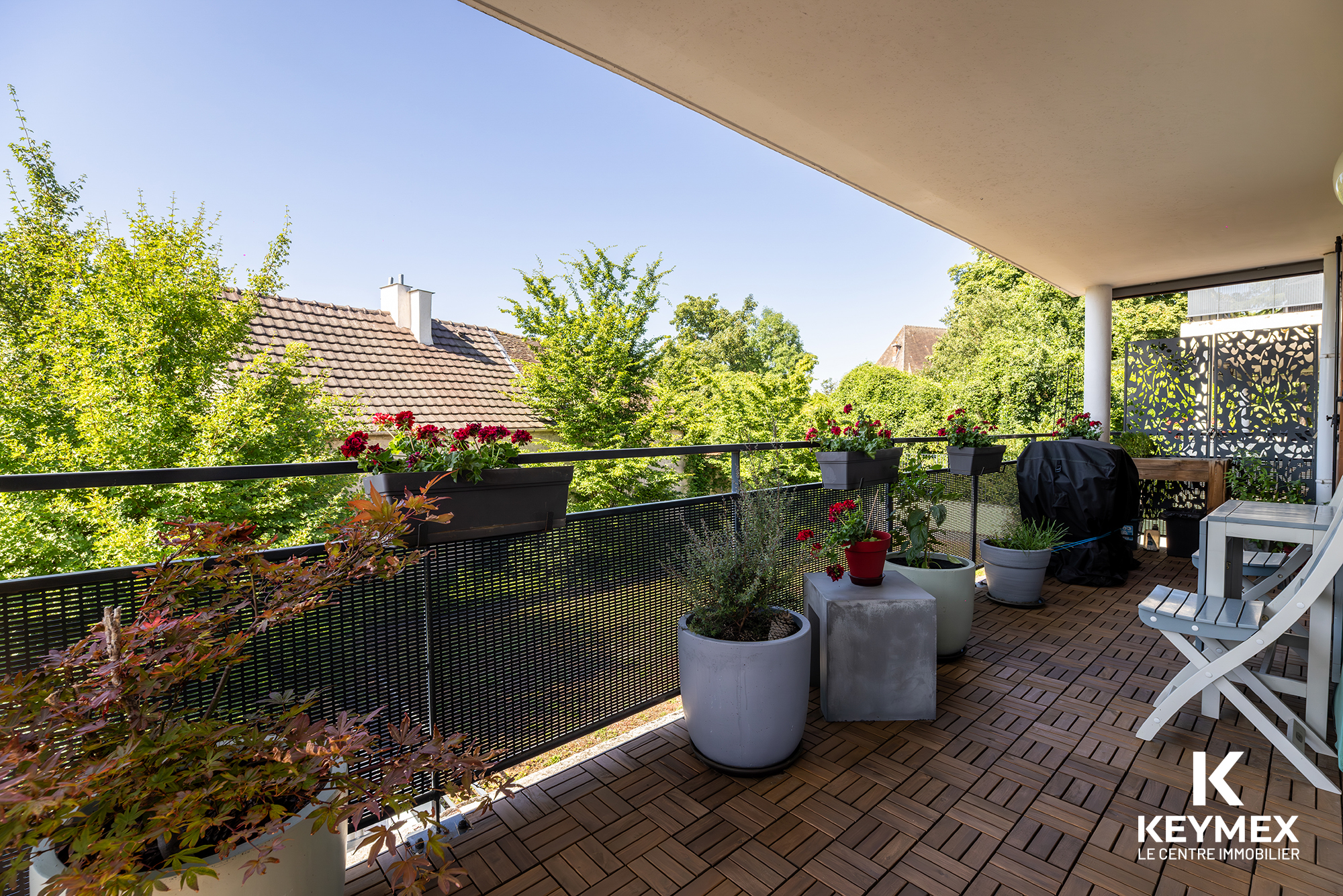 Terrasse fleurie avec vue sur arbres et maisons.