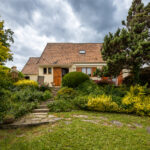 Maison avec jardin et ciel nuageux.