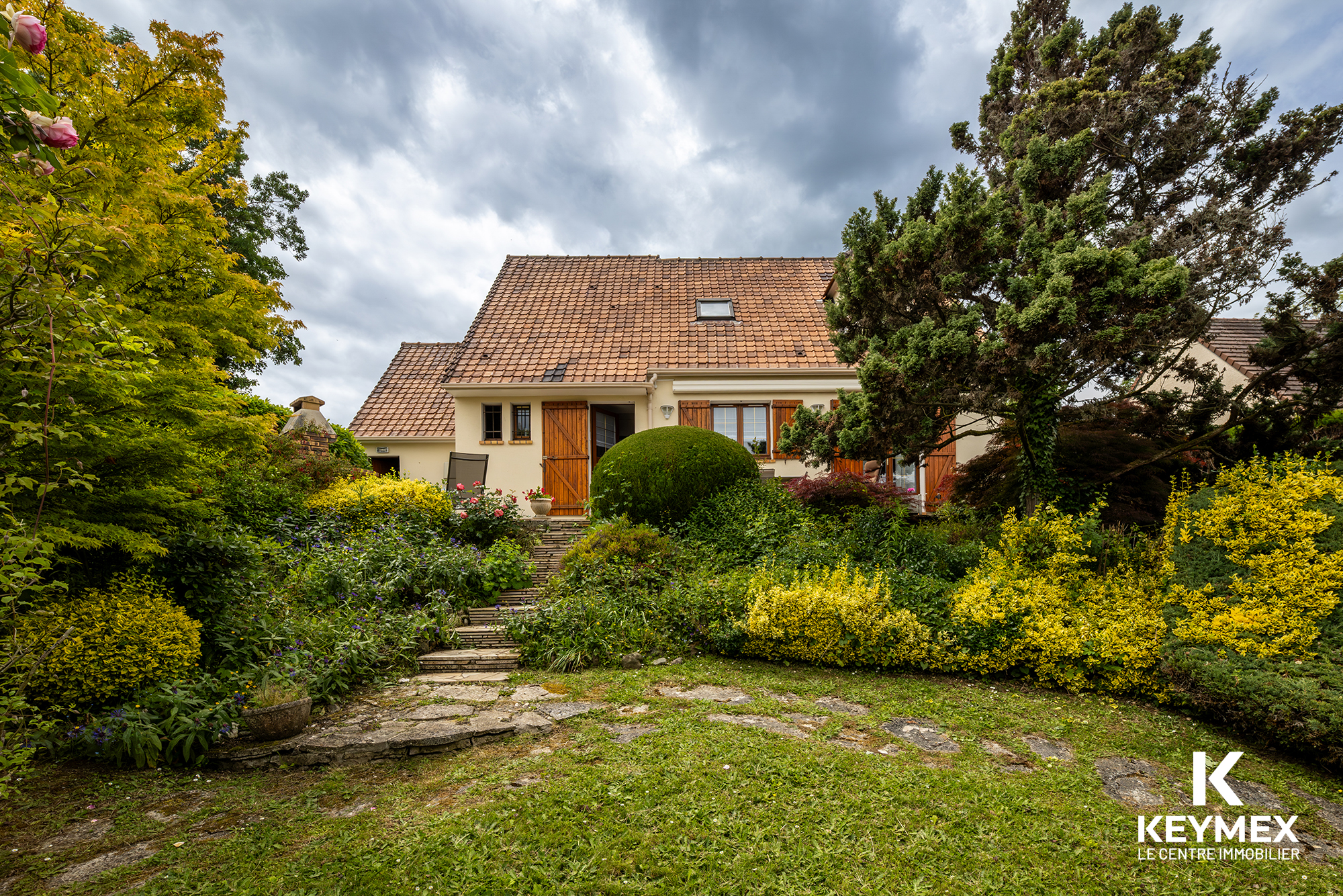 Maison avec jardin et ciel nuageux.