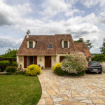 Maison avec jardin en pavé et voiture garée.