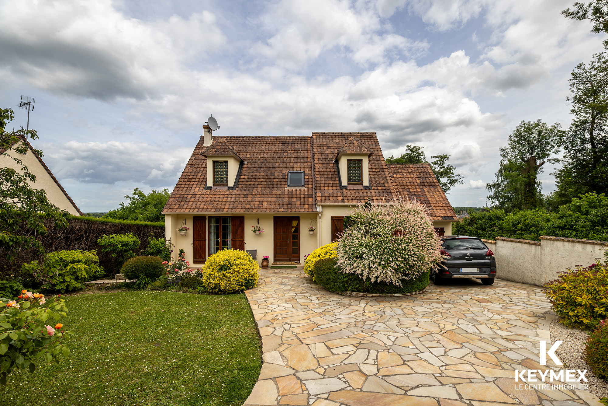 Maison avec jardin en pavé et voiture garée.