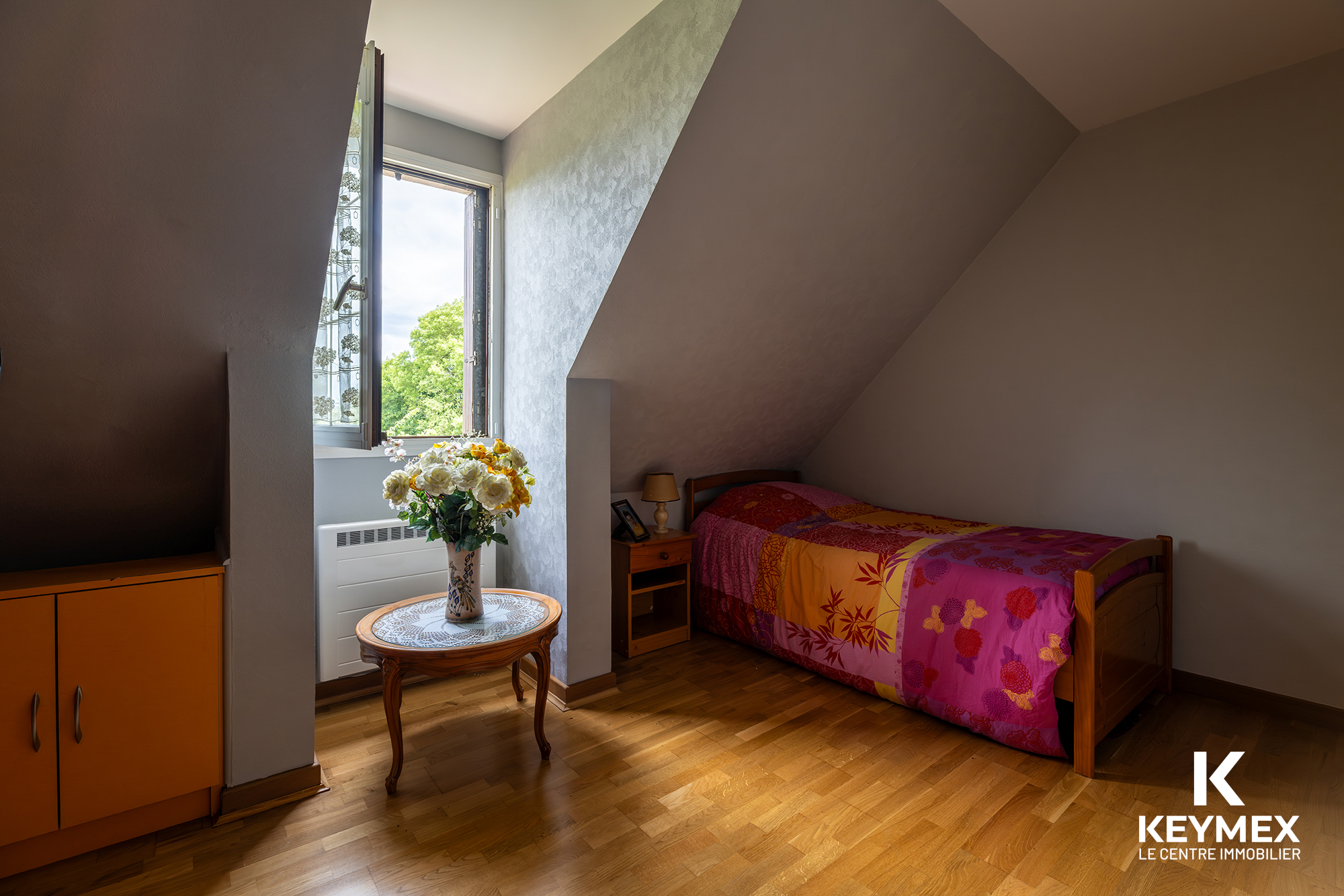 Chambre mansardée lumineuse avec lit coloré.