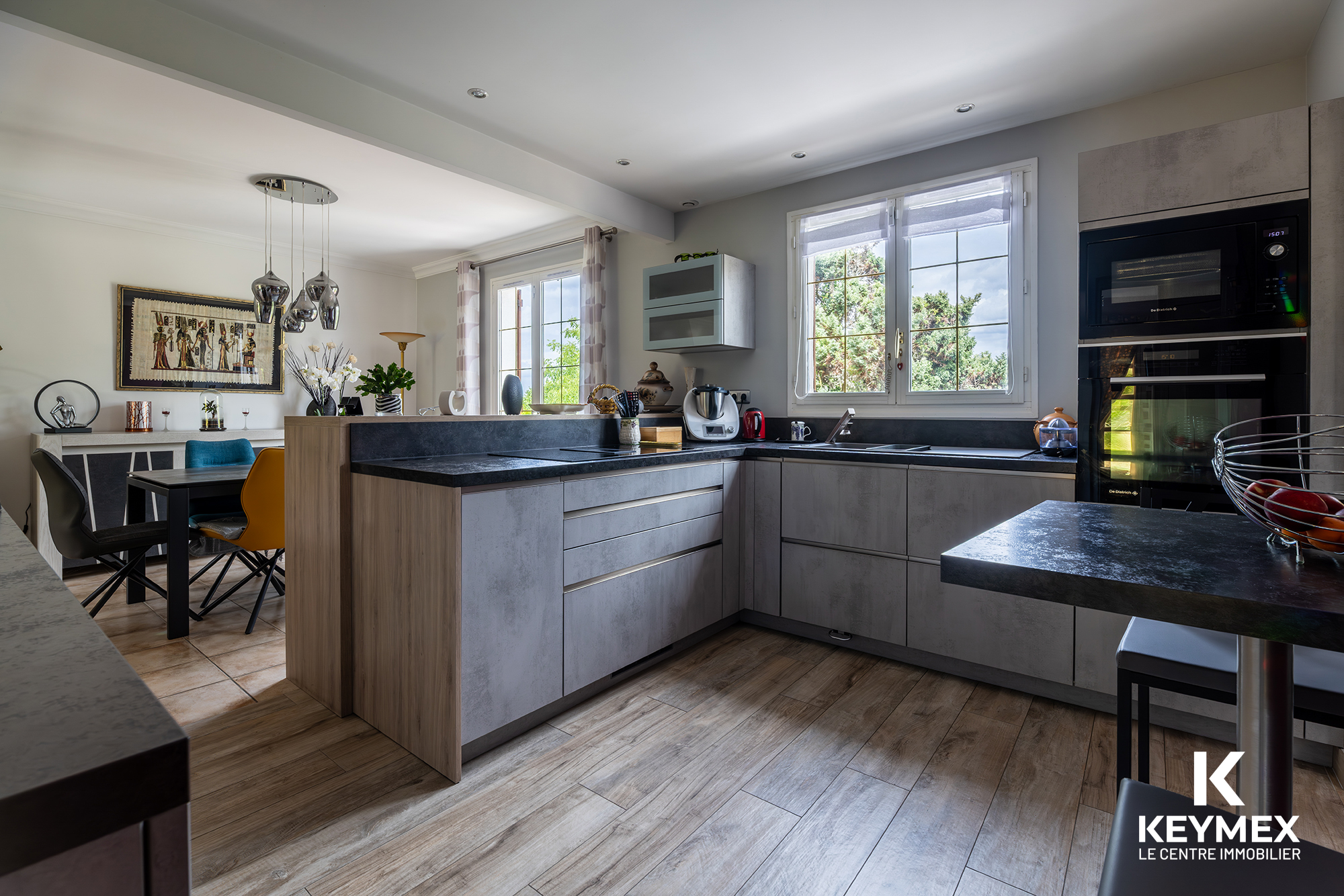 Cuisine moderne avec meubles gris et fenêtres lumineuses.