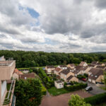 Vue aérienne de maisons et arbres sous ciel nuageux.