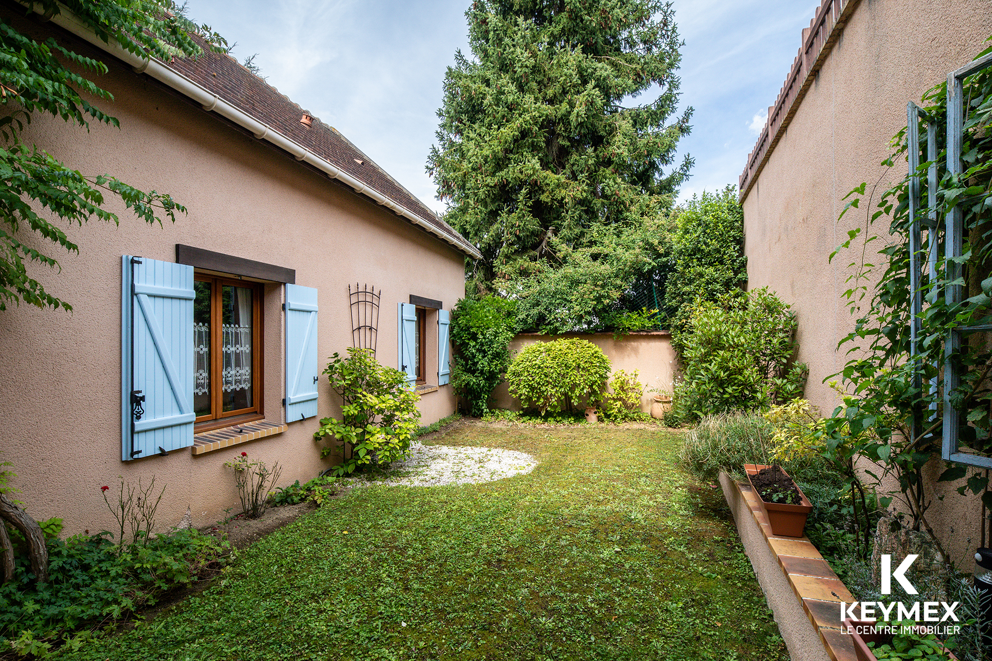 Jardin avec maison aux volets bleus en France.