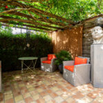 Terrasse ombragée avec mobilier en rotin et sculpture.