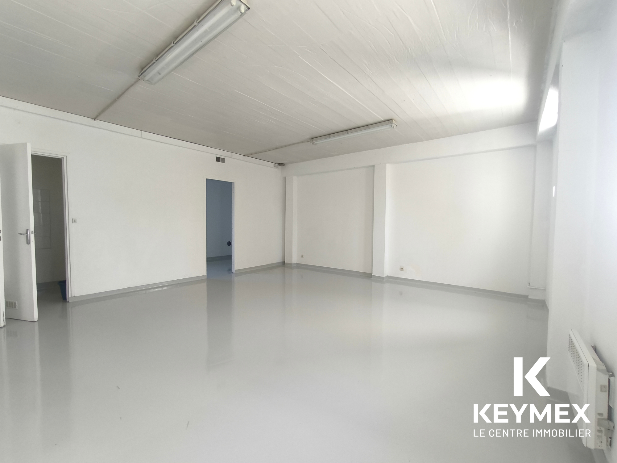 Salle vide lumineuse avec murs blancs et portes.