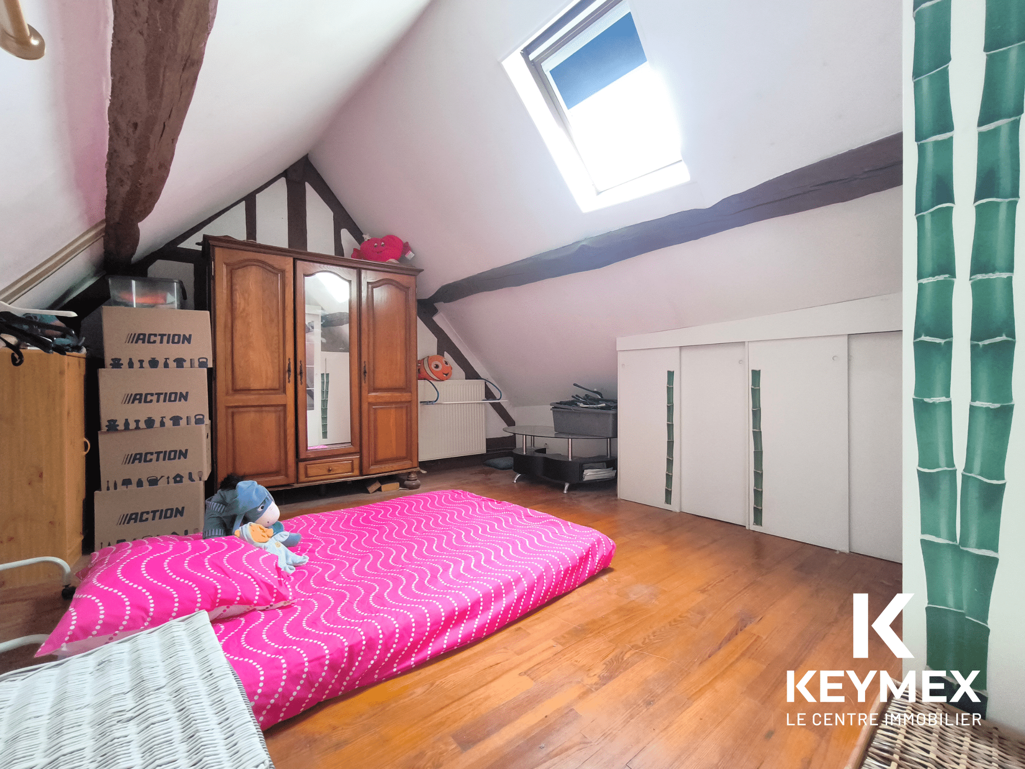 Chambre mansardée avec matelas et armoire en bois.