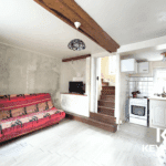 Salon lumineux avec canapé et cuisine équipée.