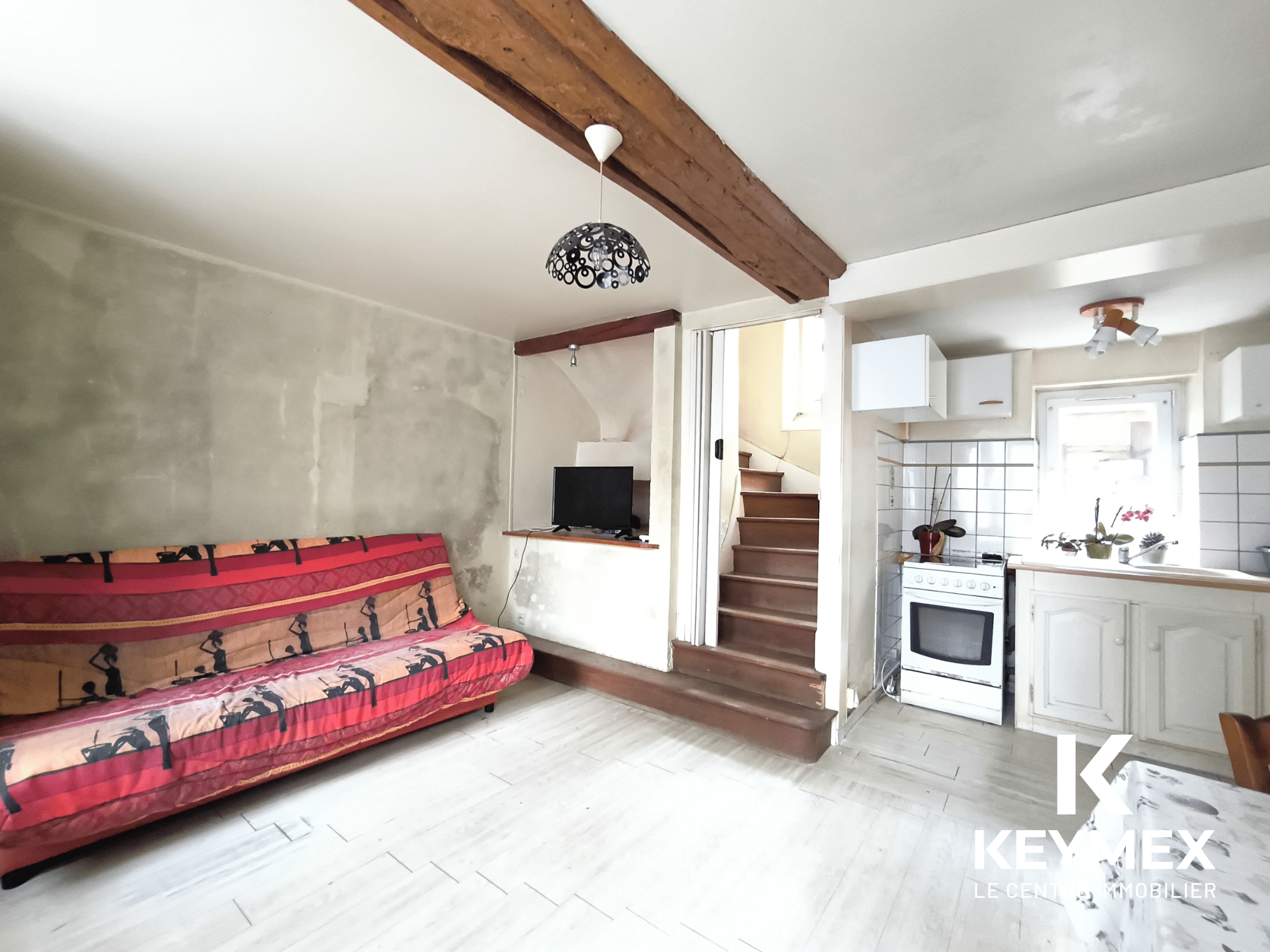 Salon lumineux avec canapé et cuisine équipée.