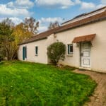 Maison avec jardin, ciel bleu et arbres.