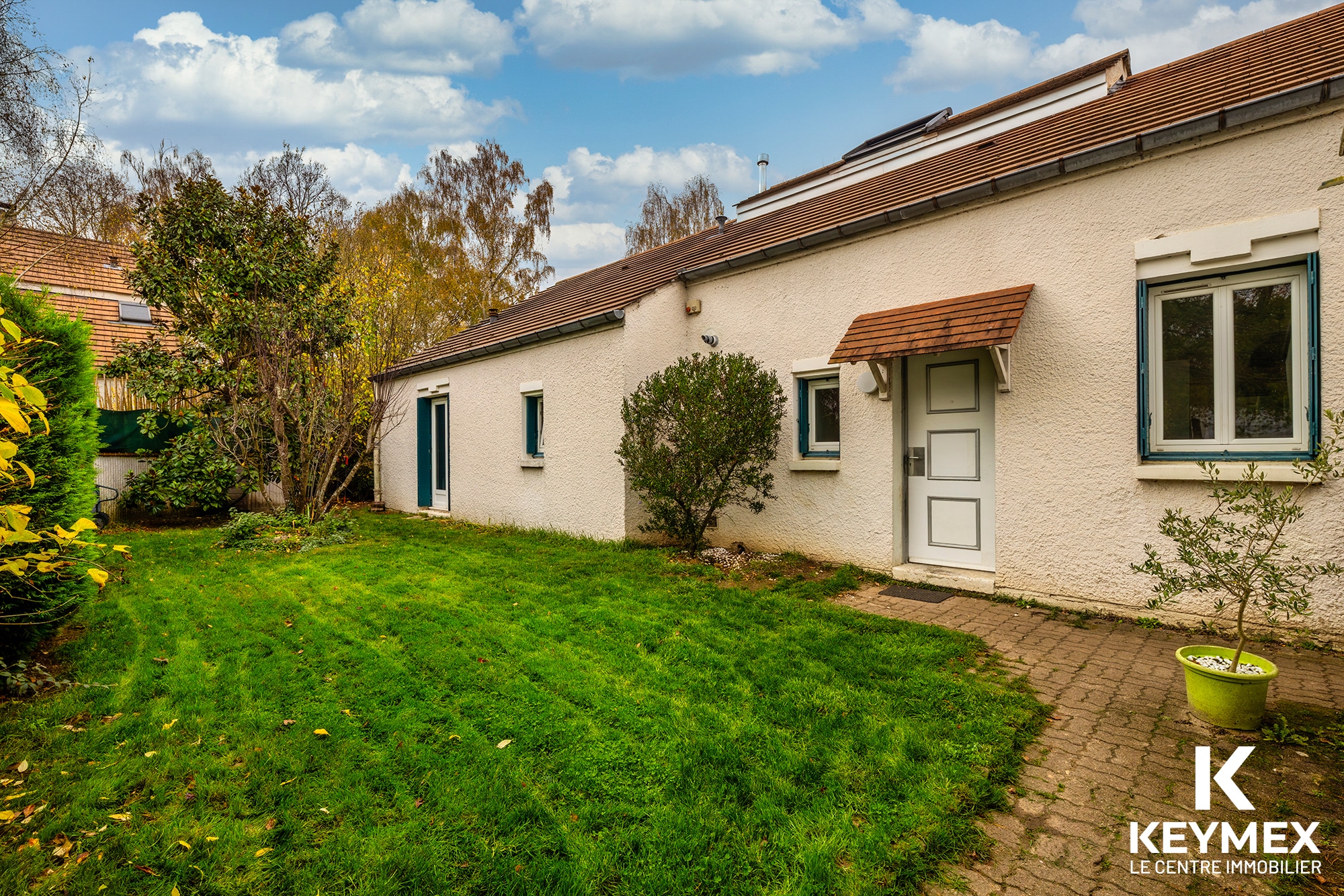Maison avec jardin, ciel bleu et arbres.