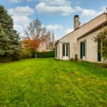 Jardin avec maison, arbres et ciel nuageux.