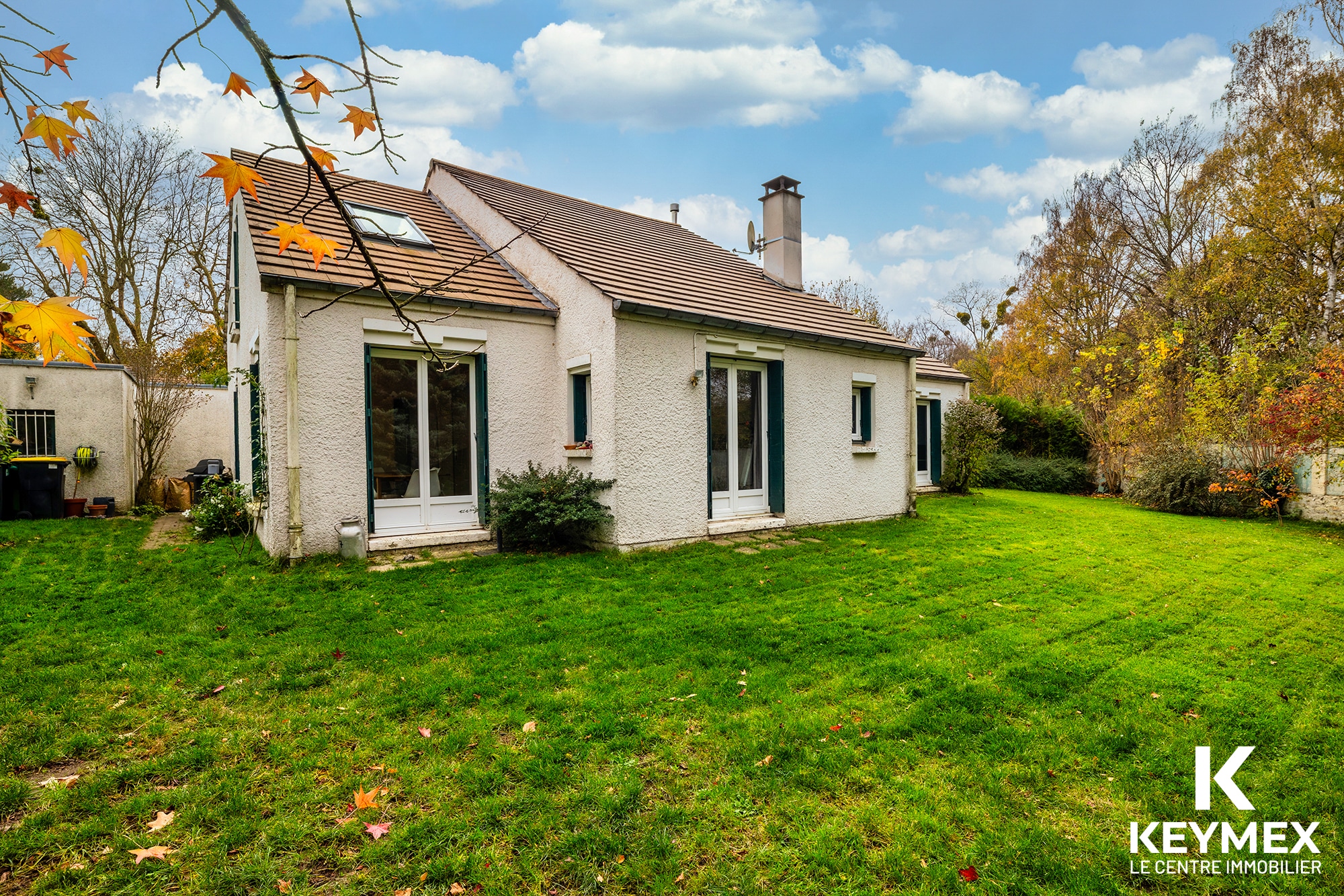 Maison avec jardin en automne, ciel bleu.