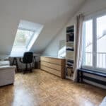 Chambre mansardée avec bureau, canapé et fenêtres.