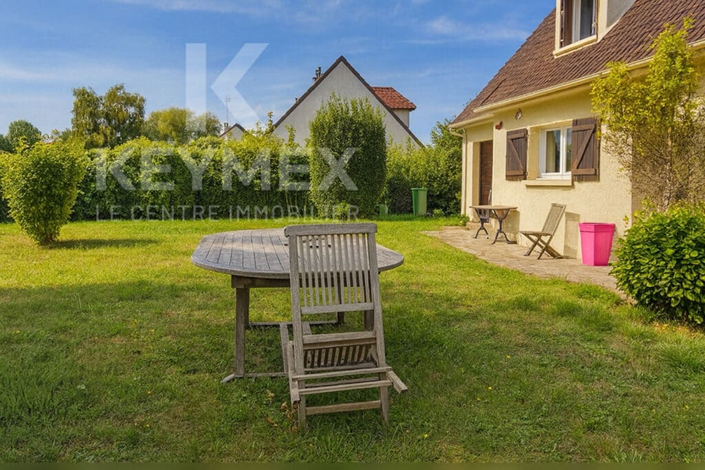 Jardin avec table en bois et maison beige.